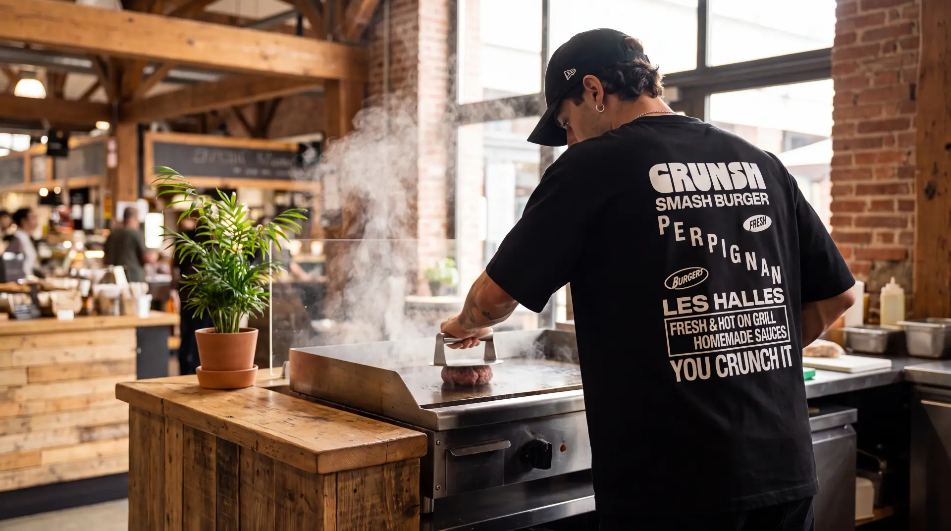 Cuisinier Crunsh de dos, t-shirt et casquette CRUNSH, en train de smasher un steak sur la plancha